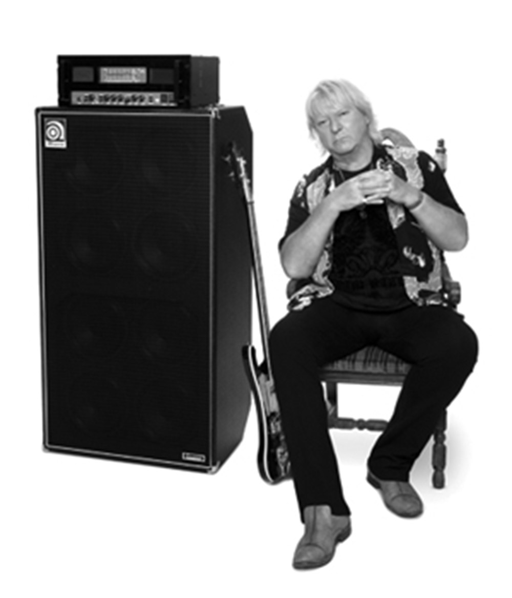 Chris Squire sitting in a chair by an Ampeg stack