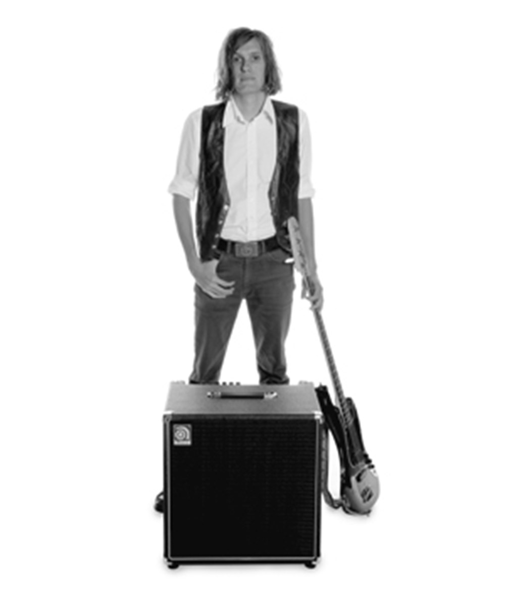 Nikolai Fraiture standing behind an Ampeg cab with his bass by his side