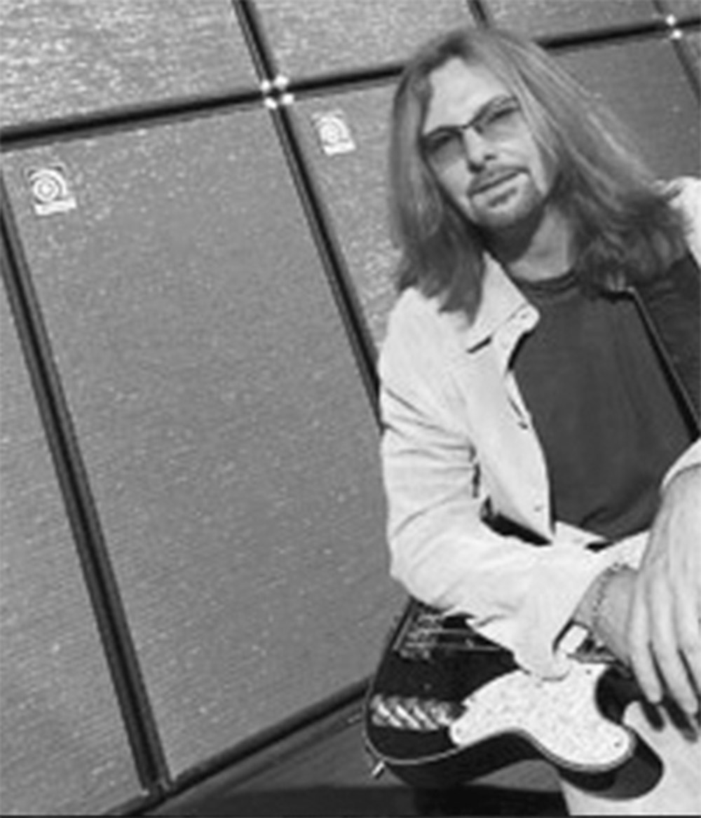 Ricky Phillips sitting on stage holding a bass