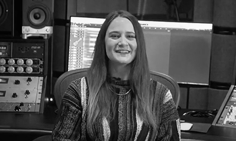 Gigi Zimmer sitting in a studio in front of mixing console and computer