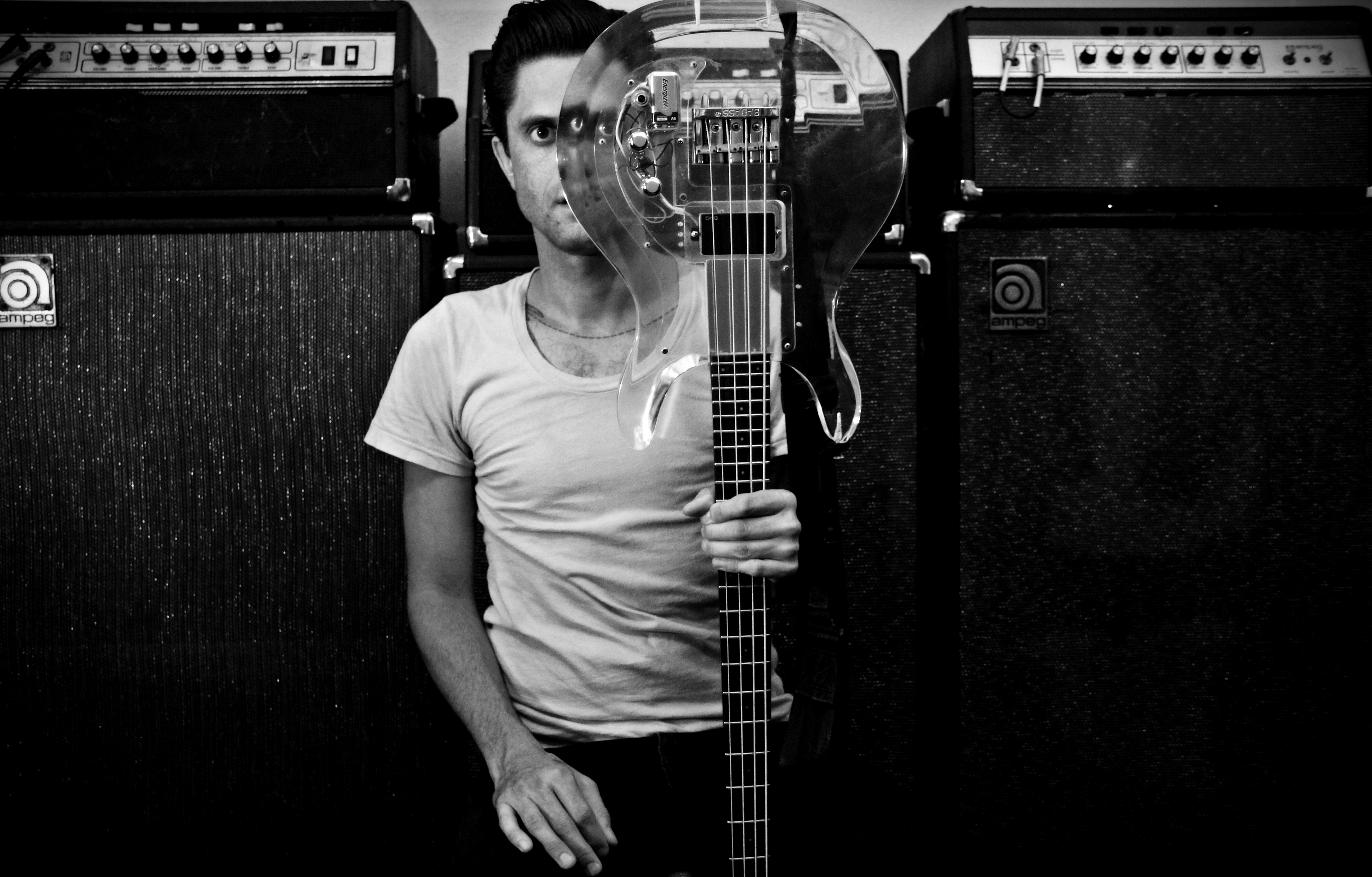 Justin Pearson holding a transparent bass in front of the left side of his face