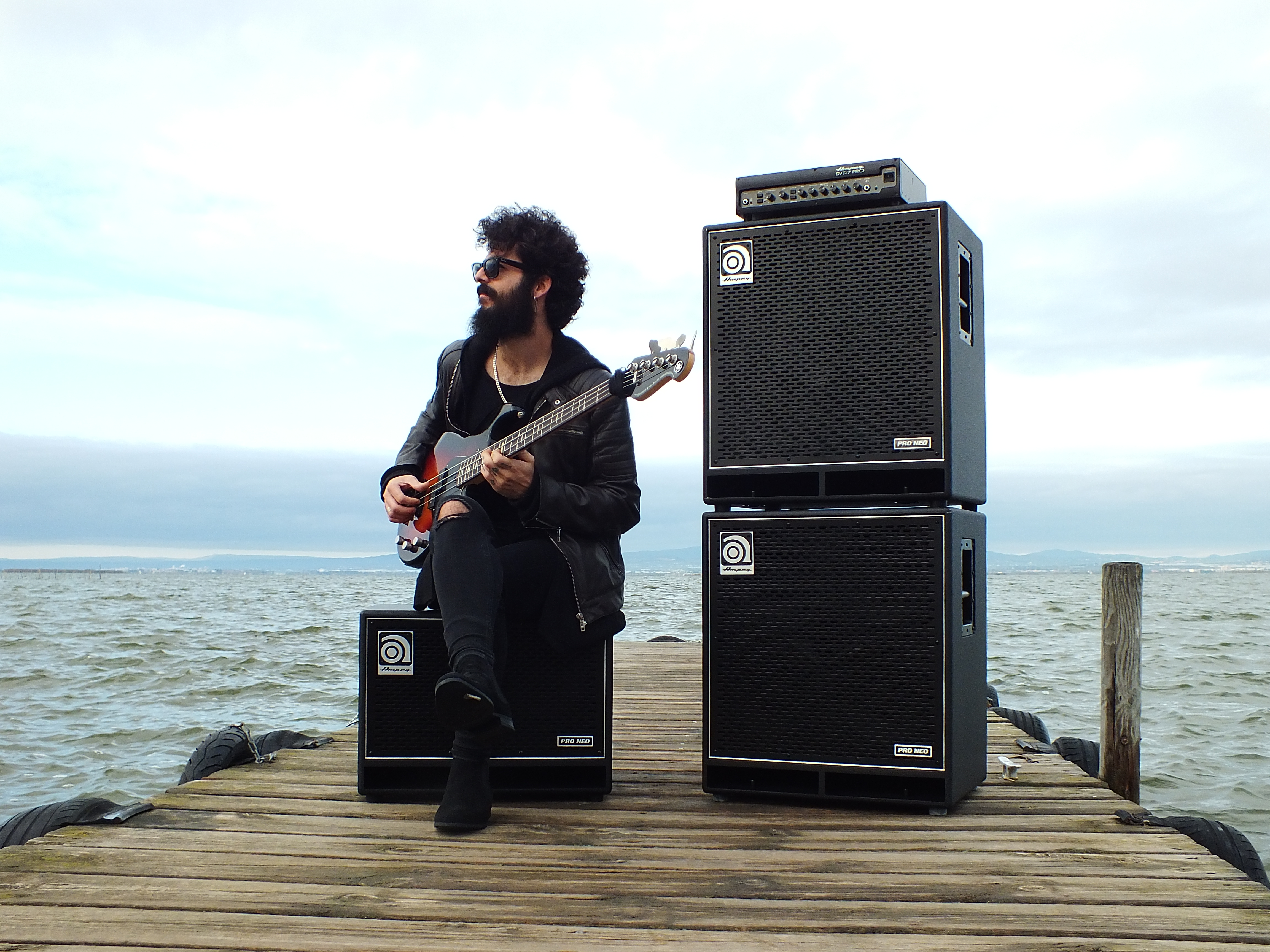 Vincen Garcia playing bass sitting on an Ampeg cab outside on a dock