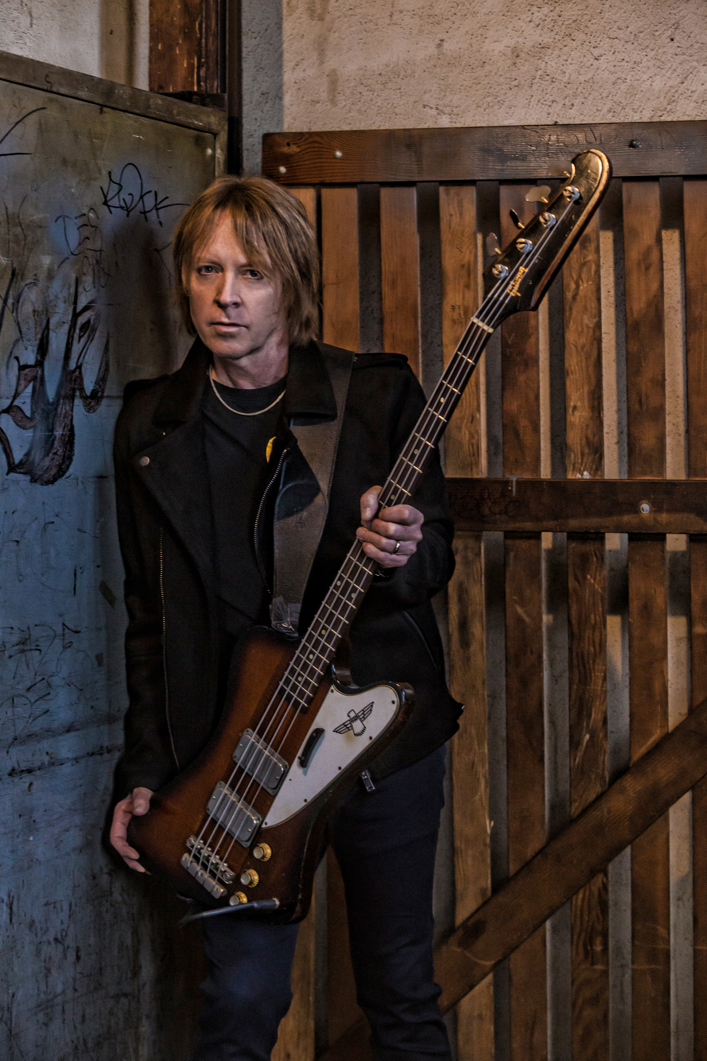 Jeff Pilson holding a bass in front of a wood fence